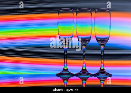 Trois verres de champagne dans une rangée avec un arc-en-ciel de couleurs de peinture de lumière derrière eux Banque D'Images