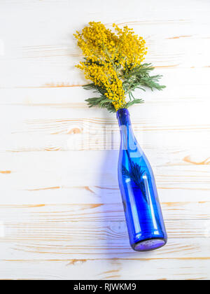 Bouquet de Mimosa dans un vase de verre bleu sur la table de bois blanc Banque D'Images