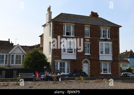 Maison victorienne située sur front de mer avec vues sur la mer. Aldeburgh, Suffolk, Angleterre, Royaume-Uni. Jeune famille de manger du poisson et frites assis sur un banc. Banque D'Images