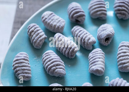 Gros plan frontal de matières gnocchi bleu sur fond blanc porcelaine bleu vintage bac italien fait avec pommes de terre gnocchi violet sur une plaque vintage turquoise Banque D'Images