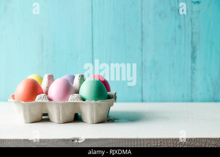 Œufs de Pâques colorés pastel dans une boîte d'oeufs en bois avec un fond bleu turquoise Banque D'Images