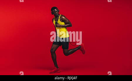 Toute la longueur de santé de la jeune homme africain en marche avec la corde à sauter sur fond rouge. Modèle de remise en forme de l'Afrique en vêtements sports en studio. Banque D'Images