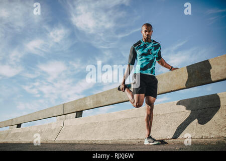 African American man in sportswear standing par la rue et l'étirement des jambes. Sportsman réchauffe avant de s'exécuter dans un matin dans la ville. Banque D'Images