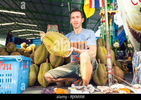 Homme voyageur tient dans la main populaire exotique fruit tropical connu pour son odeur fétid de sueur / fruits thaïlandais : Durian, roi des fruits tropicaux Banque D'Images