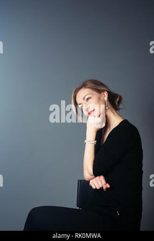 Portrait de femme belle dans une robe noire à l'arrière-plan gris Banque D'Images