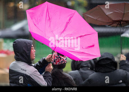 Les touristes avec leurs parapluies alors qu'ils traversent un pont pendant une douche de pluie sur une journée humide et venteux en Bourton-sur-le-Eau dans le Gloucestershire. 08.02.19. Banque D'Images