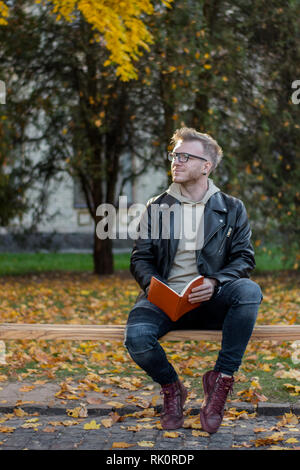 Rêver heureux guy dans les tenues de lu le livre et s'assied sur un banc de parc Banque D'Images