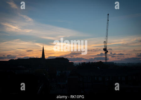 D'une grue, d'un clocher d'église et les toits de la silhouette sur un ciel magnifique au lever du soleil. Banque D'Images