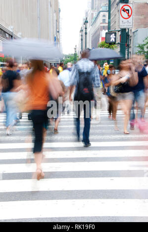 Hommes et femmes, certains tenant un parapluie, traversant une voie piétonne dans une section urbaine animée flanquée de grands bâtiments. Banque D'Images