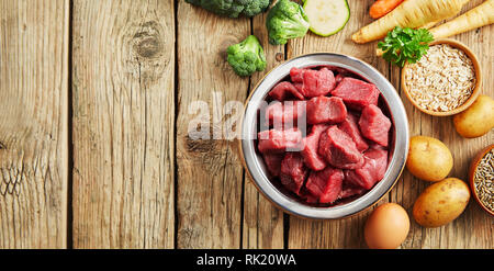 Bol de viande hachée pour un chien ou un chat sur un sol en bois rustique entouré par des légumes frais pour la santé de l'alimentation animale Banque D'Images