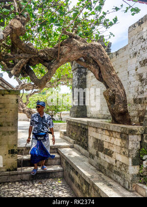 Un homme portant un sarong marcher dans une cour de temple d'Uluwatu, Bali Indonésie composé. Banque D'Images