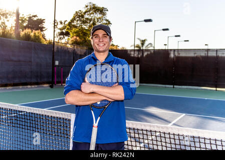 Jeune et beau professeur de tennis montrant sourire et l'expression heureuse sur le court de tennis. Banque D'Images