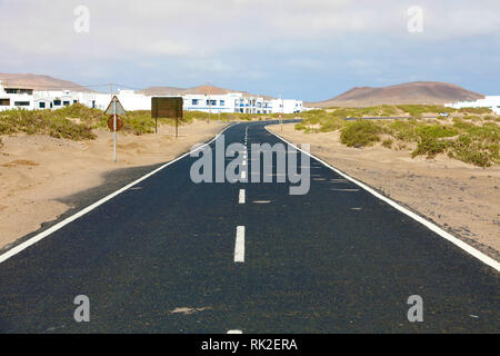 Desert route asphaltée avec un petit village typique de l'île de Lanzarote sur l'arrière-plan, Îles Canaries Banque D'Images