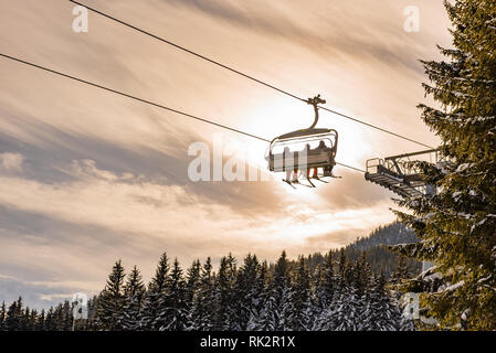 Skieurs sur un télésiège à la lumière du soleil et les arbres, photo contour orange, nuances, région de ski de Schladming, Autriche Banque D'Images