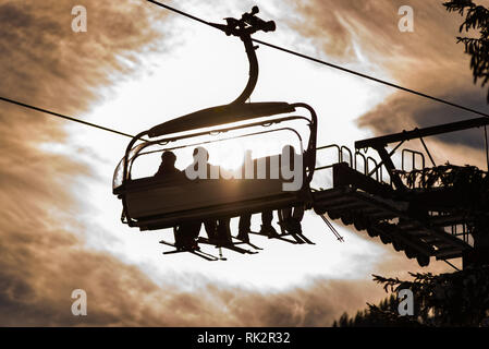 Quatre skieurs sur un télésiège à la lumière du soleil et les arbres, photo contour orange, nuances, région de ski de Schladming, Autriche Banque D'Images