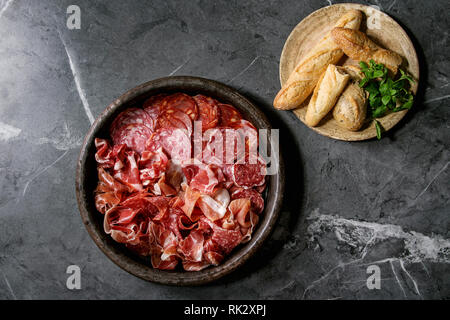 L'antipasto plateau de viande assorti de tranches de jambon, salami, saucisson chorizo dans le bac en terre cuite avec du pain et des verts sur fond noir en arrière-plan. Appartement la Banque D'Images