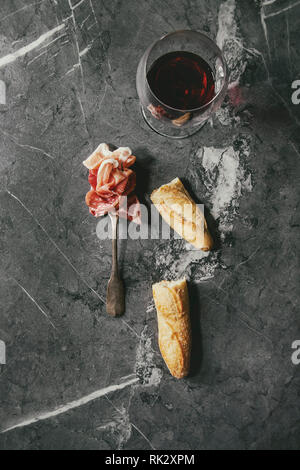 Antipasti) assorti de tranches de jambon, salami, saucisson chorizo sur fourche avec du pain et un verre de vin rouge sur fond noir en arrière-plan. Mise à plat, de l'espace Banque D'Images