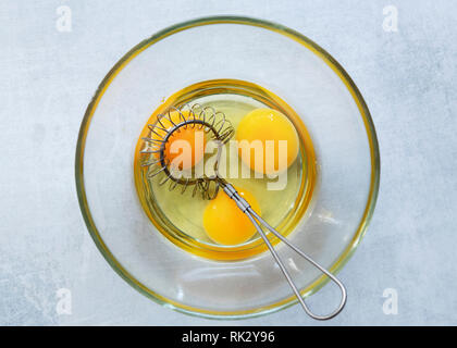 Trois oeufs crus avec un fouet dans un bol en verre. Banque D'Images