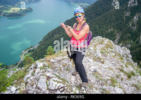 Femme climber Drachenwand ci-dessus Mondsee, Autriche, pointant vers le lac ci-dessous, après avoir suivi un parcours de via ferrata, sur une chaude journée d'été,. Banque D'Images
