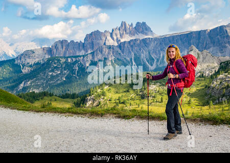 Heureux touriste debout devant un paysage majestueux, l'arrière-plan avec les bâtons de trekking dans les mains et un grand sac à dos rouge, dans la montagne des Dolomites Banque D'Images