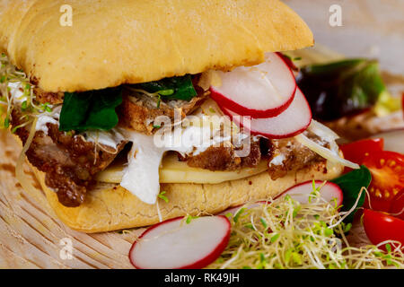 Sandwich avec de la viande, radis, oignons, fromage, sauce et laitue sur une planche en bois sur les tomates cerises. Banque D'Images