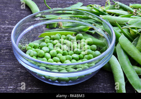 Fresh, vert pois écossés dans un bol en verre avec quelques gousses autour sur une surface en bois grunge Banque D'Images