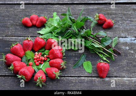 Les fraises cultivées et sauvages avec le baume de citron et feuilles de menthe sur la vieille table en bois de chêne Banque D'Images