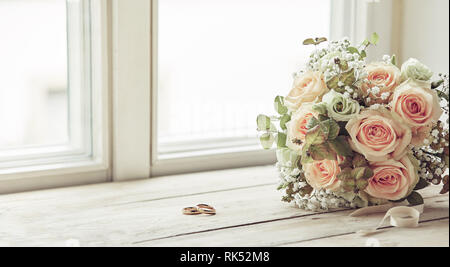 Paire de bagues de mariage et bouquet de roses roses, assis sur un rebord de fenêtre, avant la cérémonie Banque D'Images