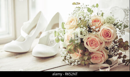 Chaussures blanches mariées et mariage bouquet de roses roses de en close-up sur les bas de caisse en bois de fenêtre lumineuse Banque D'Images