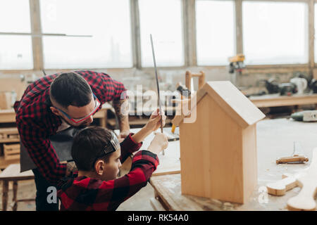 Carpenter l'édification d'une cabane en bois avec son enfant. Un petit fils participe activement au processus de la main. Professionnels de la paternité et DIY con Banque D'Images