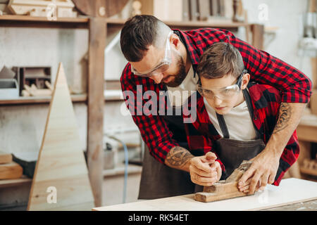 Carpenter peu apprenti ou élève en avion à l'aide de lunettes de sécurité lorsque vous travaillez avec la planche en bois en atelier. Banque D'Images