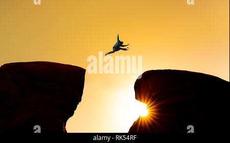 Défi, le risque et la liberté concept. Une Silhouette man jumping over précipice crossing cliff Banque D'Images