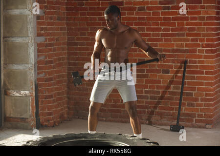 L'homme musclé de frapper avec un marteau pneumatique roue traîneau, l'exécution de l'exercice crossfit lorsqu'une perte de l'excès de poids est plusieurs fois plus élevé que le débit Banque D'Images
