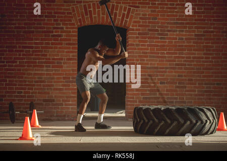 L'homme musclé de frapper avec un marteau pneumatique roue traîneau, l'exécution de l'exercice crossfit lorsqu'une perte de l'excès de poids est plusieurs fois plus élevé que le débit Banque D'Images