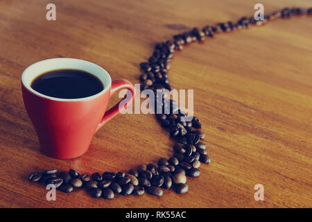 La tasse est rouge sur la table en bois, les grains de café sont disposés avec une ligne courbe Banque D'Images