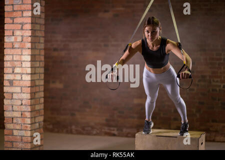 Jeune femme séduisante avec formation de remise en forme dans les sangles trx studio crossfit, systèmes de suspension de cordes ou de courroies qui permettent d'effectuer des sportgirl e Banque D'Images