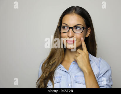 Jeune belle brunette businesswoman smiling à sur le côté et en pointant le doigt sur sa joue sur fond blanc Banque D'Images