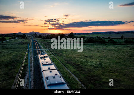 Long des voies de chemin de fer avec motion blurred train électrique, vue de l'un pont au-dessus de l'été au coucher du soleil derrière les nuages colorés, photo prise près de Krum, Bulgarie Banque D'Images