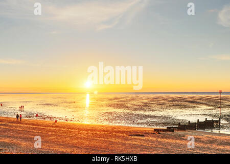 Coucher du soleil sur la Hunstanton Wash. Personnes promenade le long de la plage de Hunstanton, Norfolk, England, UK, comme le soleil se couche à l'ouest sur la mer. Banque D'Images