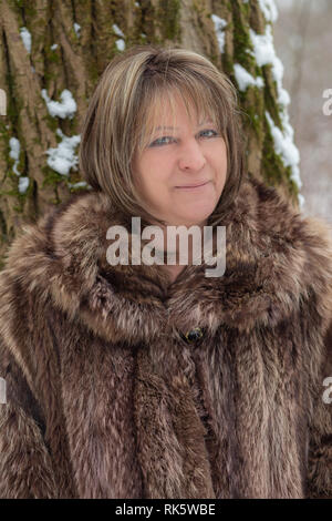 Femme mature en manteau de fourrure à l'extérieur à la caméra en souriant Banque D'Images