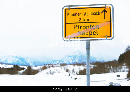 Panneau de circulation jaune avec des noms de ville. Paysage d'hiver avec des montagnes sur l'arrière-plan. Pfronten en Bavière, Allemagne. Banque D'Images