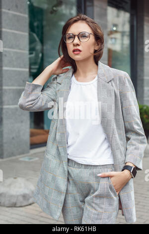 D'affaires décontractée. Jeune femme à lunettes marche sur la ville main street dans la poche des Banque D'Images