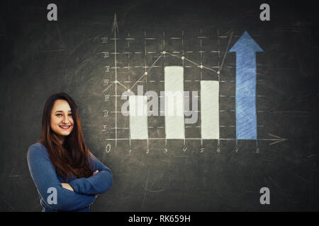 Pretty woman holding analyste les bras croisés devant un immense tableau noir avec un graphique tiré de plus en plus avec des flèches. Les industries profitent d'affaires Banque D'Images