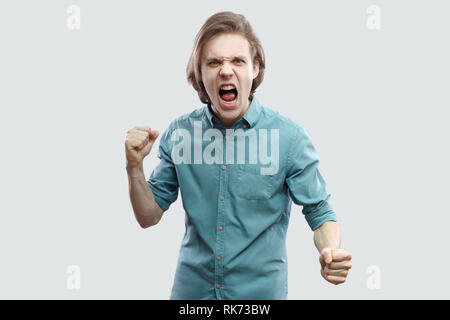 Portrait de fou furieux beau jeune homme blond aux cheveux longs en bleu chemise décontractée debout, looking at camera, criant et prêt à l'attaque. Banque D'Images