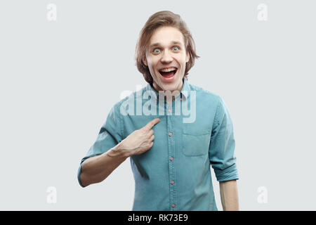 Portrait d'étonné surpris beau jeune homme blond aux cheveux longs en bleu chemise décontractée de pointage permanent lui-même et ne peuvent pas croire. Piscine studio s Banque D'Images