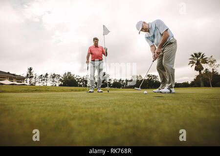 Low angle view of senior golfeur sur putting green sur le point de prendre la photo. Homme joueur de golf putting on vert avec deuxième joueur masculin dans l'arrière-plan h Banque D'Images