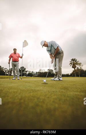 Les golfeurs professionnels jouer au golf ensemble sur le cours. golfeur aîné en effectuant une prise sur le green avec autre joueur debout dans l'arrière-plan vertige Banque D'Images
