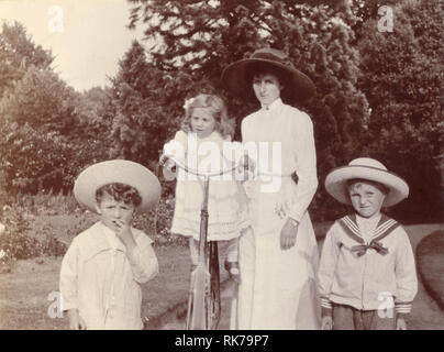 Original Vintage Cycling Edwardian photo de groupe d'une belle mère dans un chemisier blanc d'été et jupe marchant avec ses enfants dans le parc ou un jardin. Le plus jeune enfant est équilibré sur la bicyclette de la mère, les garçons portent des costumes de marin à la mode et des chapeaux de paille, vers 1910, Royaume-Uni Banque D'Images