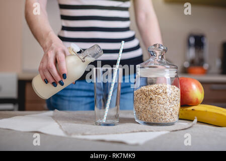 Une femme verse le lait d'avoine bio une bouteille dans un verre dans la cuisine. Produit végétarien sain de régime Banque D'Images