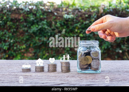 L'argent d'épargne de la vie familiale des concepts. Main tenant une pièce de monnaie sur l'argent dans un bocal en verre et membre de la famille, voiture, maison, sains sur les monnaies. Montre l'enregistrement Banque D'Images